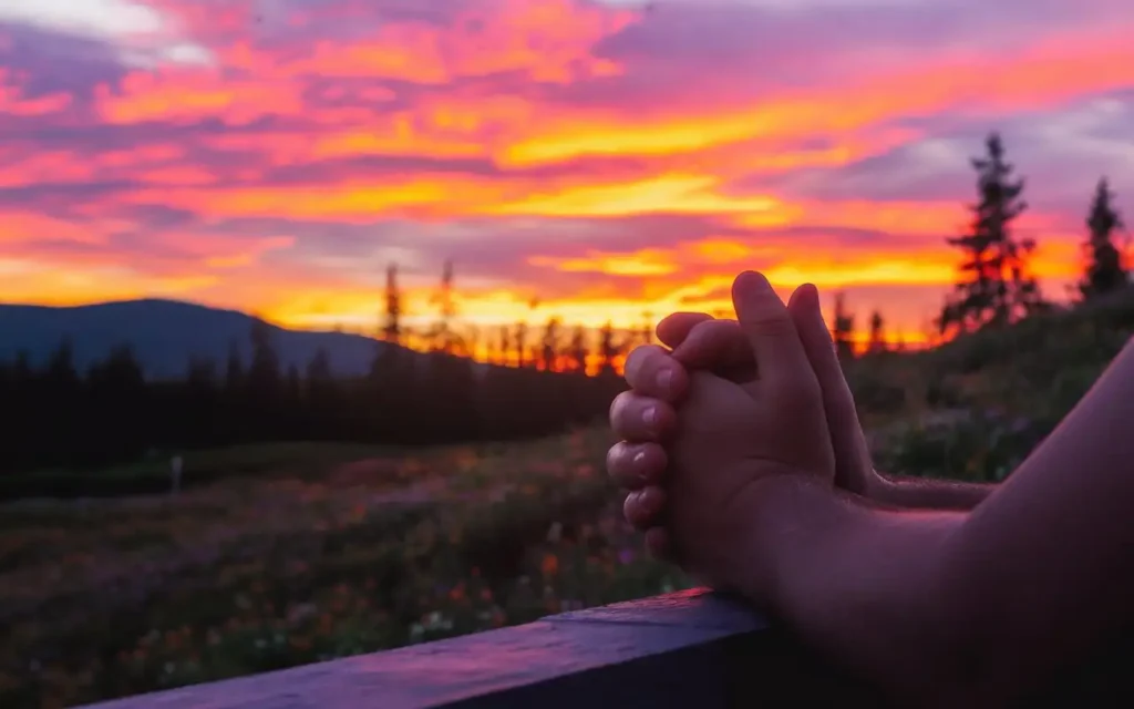 Silhouette of hands clasped in prayer during sunset
