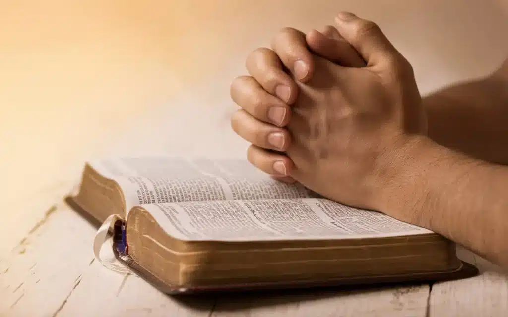 A person in prayer with hands folded over an open Bible, symbolizing the spiritual focus of fasting.